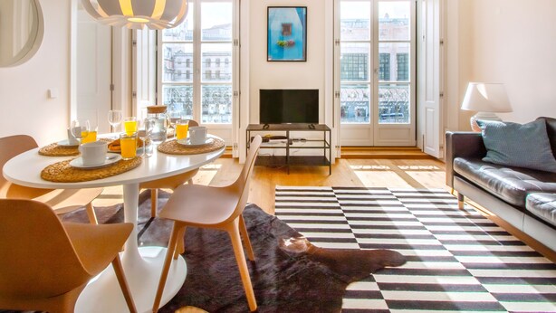 Un soggiorno moderno con zona pranzo, divano, televisione e ampie finestre con vista sulla città.