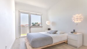 A modern bedroom with a bed, bedside tables, and a view of the outdoors through a sliding door. - Graça Amazing River Views (Lisbon)