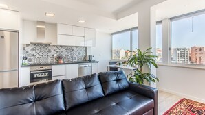 A modern apartment with a kitchen, a black leather sofa, and large windows offering a city view. - Graça Amazing River Views (Lisbon)