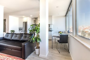 A modern living room with a leather sofa, a dining area, and a view of a cityscape through large windows.