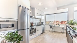 A modern kitchen with stainless steel appliances, a dining area with a view, and a black leather sofa. - Graça Amazing River Views (Lisbon)
