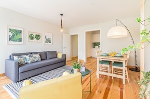 A modern living room with a grey sofa, a yellow armchair, a dining table set with plates and glasses, and a pendant light. - Santos Green Apartment (Lisbon)