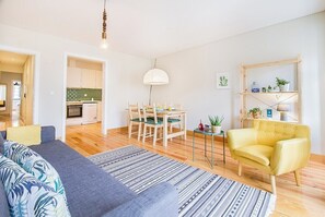 A modern living room with a sofa, a yellow armchair, a dining table with chairs, a hanging light fixture, and a kitchen in the background. - Santos Green Apartment (Lisbon)