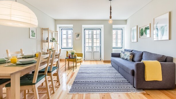 Un soggiorno moderno con zona pranzo, pavimento in legno e un divano grigio con una coperta gialla.