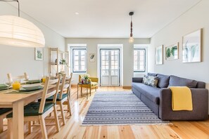 Un salon moderne comprenant un coin repas, un parquet et un canapé gris agrémenté d’un plaid jaune.