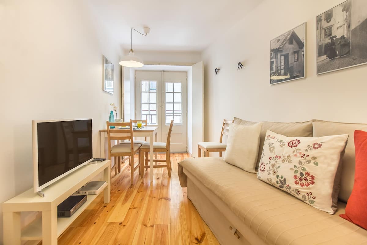 Una sala de estar con televisor, muebles de madera, un sofá con cojines estampados y una zona de comedor con mesa y sillas.