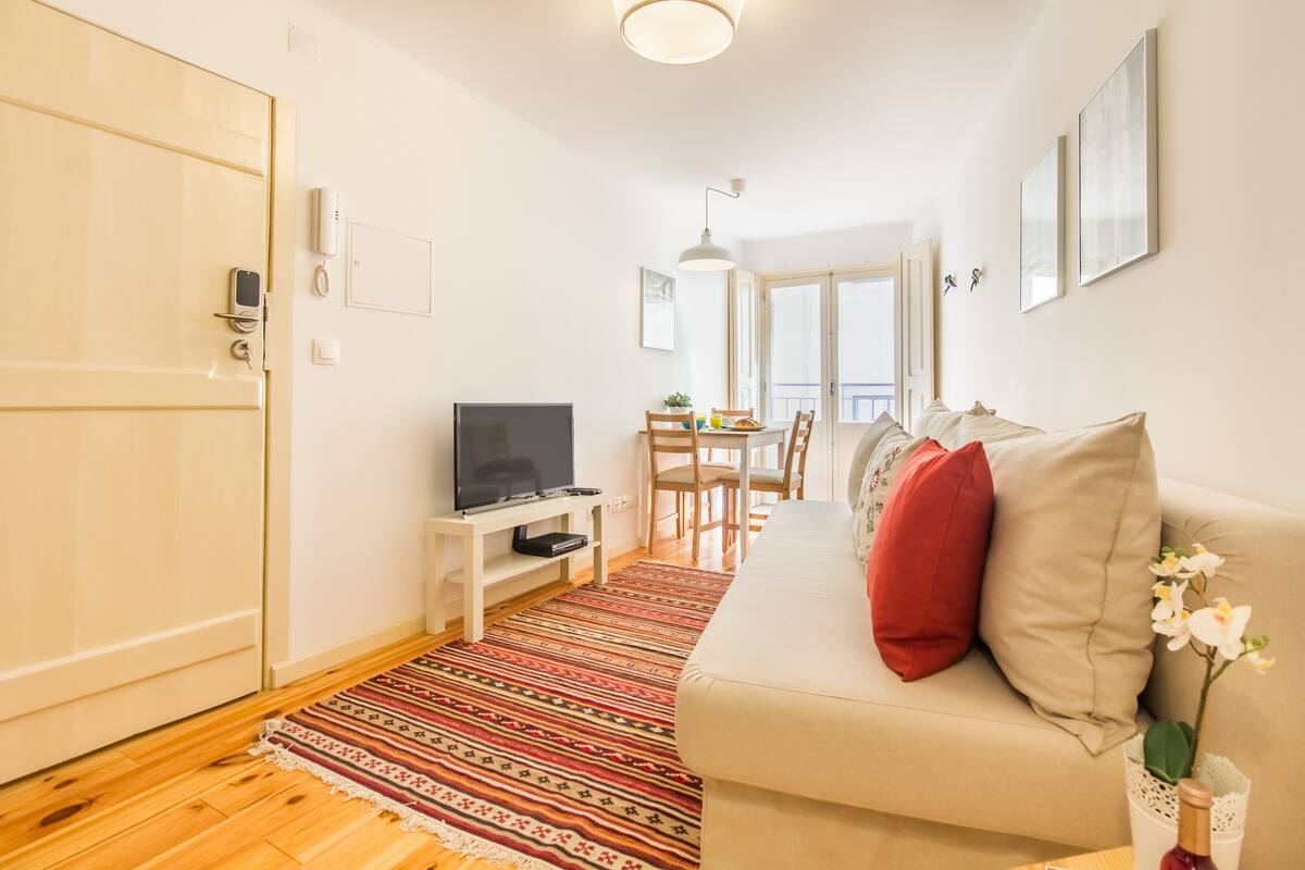 Un espacio habitable compacto con sofá, televisión, zona de comedor y una puerta con teléfono.