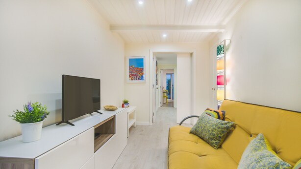 A modern living room with a flat-screen TV, a yellow sofa, and a potted plant.
