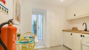 A compact kitchen with white cabinets, a wooden countertop, and a yellow chair.