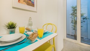 A dining table with plates, cutlery, a glass of orange juice, a bottle, and a bowl of cookies. There is a potted plant and a yellow chair.
