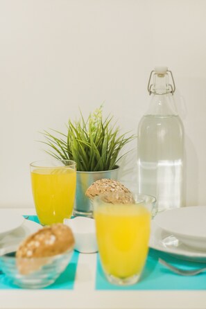 Una mesa con dos vasos de líquido amarillo, una botella de agua, una planta pequeña y una galleta.