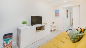 A modern living room with a flat-screen TV, white cabinetry, a yellow sofa, and a small table with decorative items.
