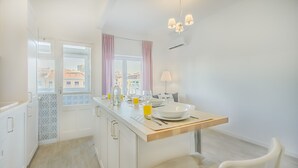 A modern kitchen with white cabinetry, a wooden countertop, and a view of the city through large windows. - Roma Cozy Flat (Lisbon)