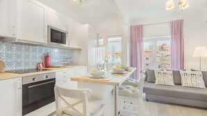 A modern kitchen with white cabinets, a microwave, and a dining area with a table and chairs. - Roma Cozy Flat (Lisbon)