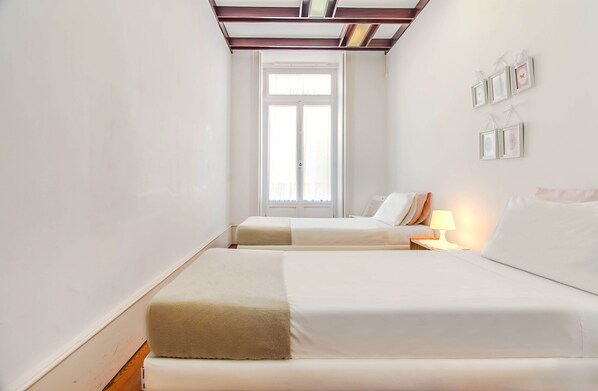 Un dormitorio con dos camas, una ventana y una lámpara fijada a la pared.