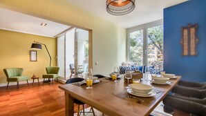 A dining area with a wooden table set for four, a sofa, and a chair. - 347 Acácias Flat (Cascais)