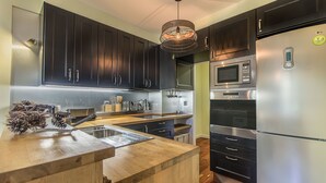 A modern kitchen with dark cabinets, stainless steel appliances, and a wooden countertop. - 347 Acácias Flat (Cascais)