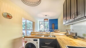 A modern kitchen with a built-in washer and dryer, wooden countertops, and a large window offering a view of the outdoors. - 347 Acácias Flat (Cascais)
