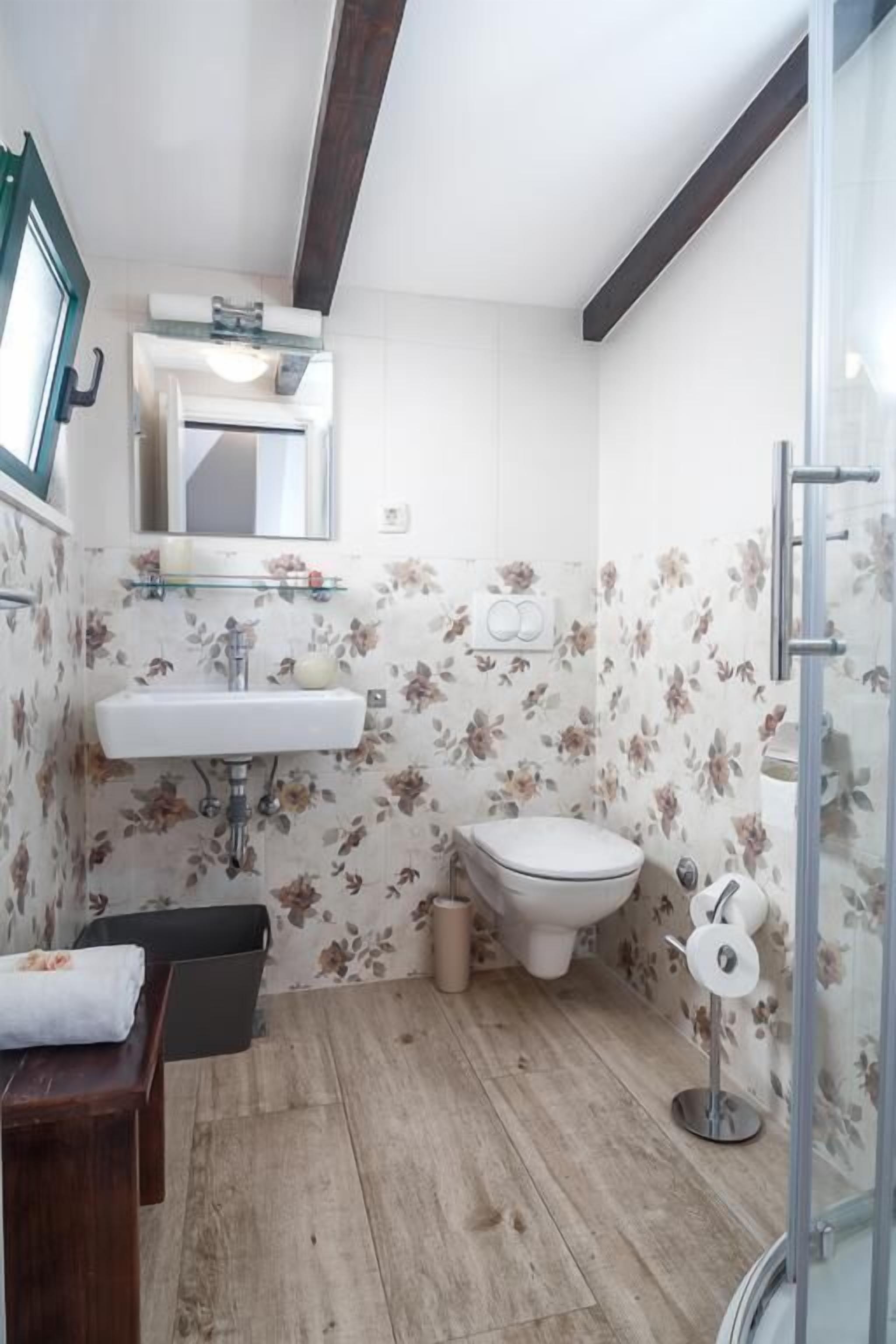 A bathroom with a wooden floor, a white sink, a toilet, and a shower area.