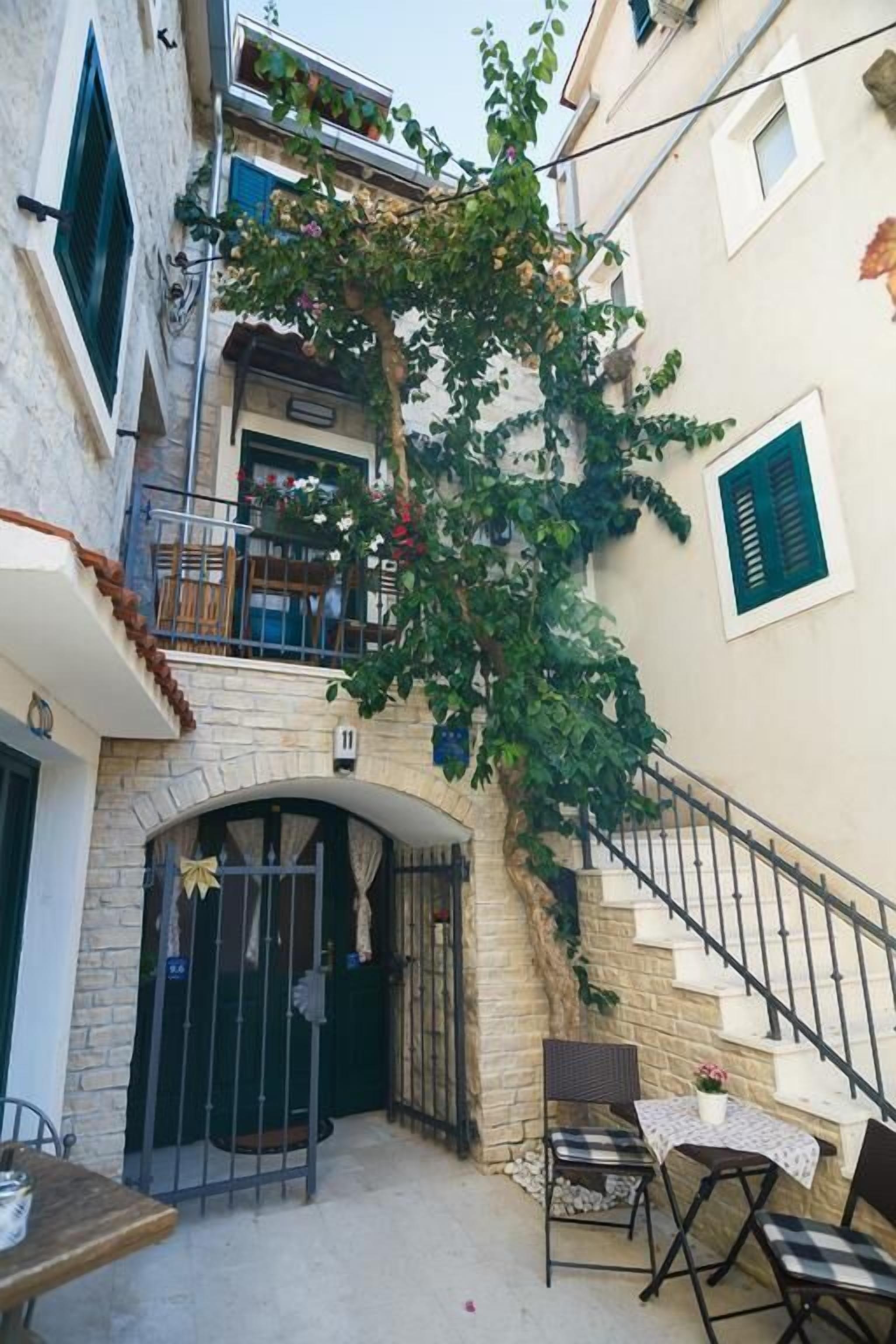Ein Innenhof mit Treppe, einem kleinen Tisch mit Stühlen und einem Baum mit grünen Blättern.