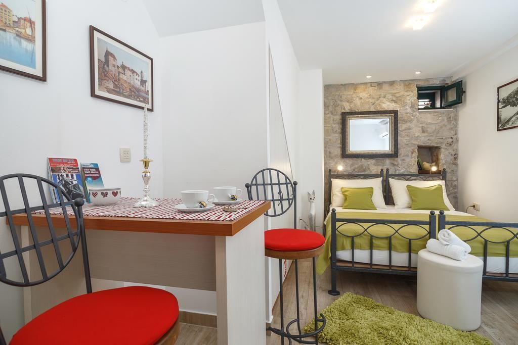 A compact bedroom with a bed, a small table with chairs, a mirror, and a stone wall.