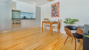 A modern kitchen with white cabinets, a wooden dining table, and a black chair. - Graça Cozy Duplex (Lisbon)