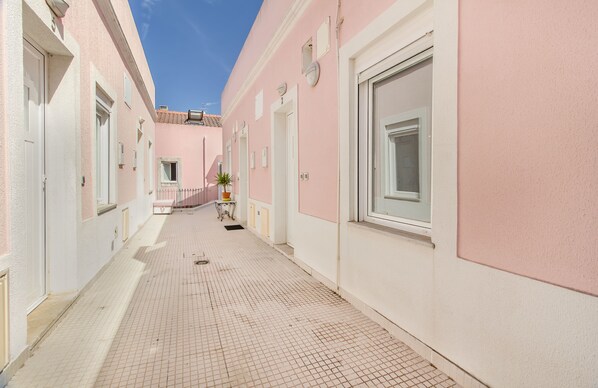 Un estrecho pasillo con baldosas, con edificios de color rosa y blanco, puertas y ventanas.