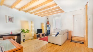 A modern living room with wooden beams, a sofa, a TV, a bookshelf, and a dining area. - Graça Cozy Duplex (Lisbon)