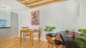 A modern kitchen with white cabinets, a wooden dining table with chairs, and a black countertop with a plant and a bottle. - Graça Cozy Duplex (Lisbon)
