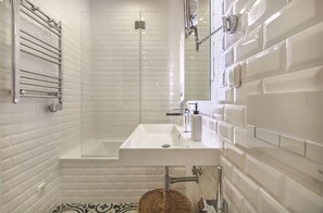 Ein modernes Badezimmer mit Dusche in weißen Fliesen, einem rechteckigen Waschbecken und einer gläsernen Duschkabine.