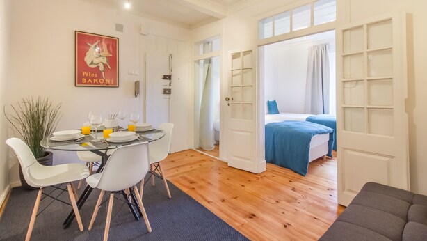 A modern room with a dining area, a bed with a blue bedspread, and a large window. - Lisbon City Stay Largo do Carmo (Lisbon)