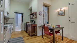 A compact kitchen with white cabinets, a wooden dining table, and a red chair. A clock and a framed photo adorn the wall. - Correeiros Downtown - Historic Lisbon Apartment (Lisbon)