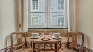 A corner seating area with a table set for tea, two chairs, and a view of a building through a window. - Correeiros Downtown - Historic Lisbon Apartment (Lisbon)
