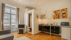 Un espace de vie compact comprenant un coin cuisine, un canapé, une table à manger et une vue dégagée sur l’extérieur grâce à une grande fenêtre.