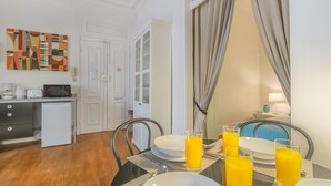 Un coin repas avec une table mise pour le petit-déjeuner, comprenant des assiettes, des verres et un verre de jus d’orange. On peut voir un four à micro-ondes et une machine à café sur le comptoir.
