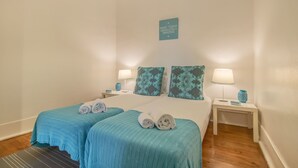 Une chambre d’hôtel avec deux lits, chacun recouvert d’une couvre-lit turquoise et agrémenté d’oreillers assortis. Il y a deux tables de chevet avec des lampes et des vases décoratifs. Un message inspirant est affiché sur le mur.