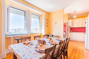 Un comedor con una mesa dispuesta para cuatro, una ventana con persianas, y una cocina al fondo.