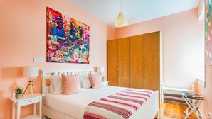 Een slaapkamer met een bed, nachtkastjes, een kledingkast en een kleurrijk abstract schilderij aan de muur.