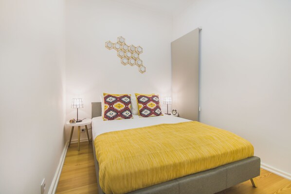 A bedroom with a bed, two bedside lamps, a wall-mounted light fixture, and a wooden floor. - Graça Trendy Flat (Lisbon)