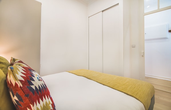 A bedroom with a bed, a colorful pillow, a yellow throw blanket, and a white wardrobe. - Graça Trendy Flat (Lisbon)