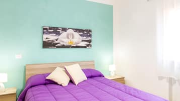 Ein Schlafzimmer mit einer türkisfarbenen Wand, einem Bett mit violetter Bettwäsche, einem Gemälde einer weißen Orchidee und zwei Nachttischlampen.