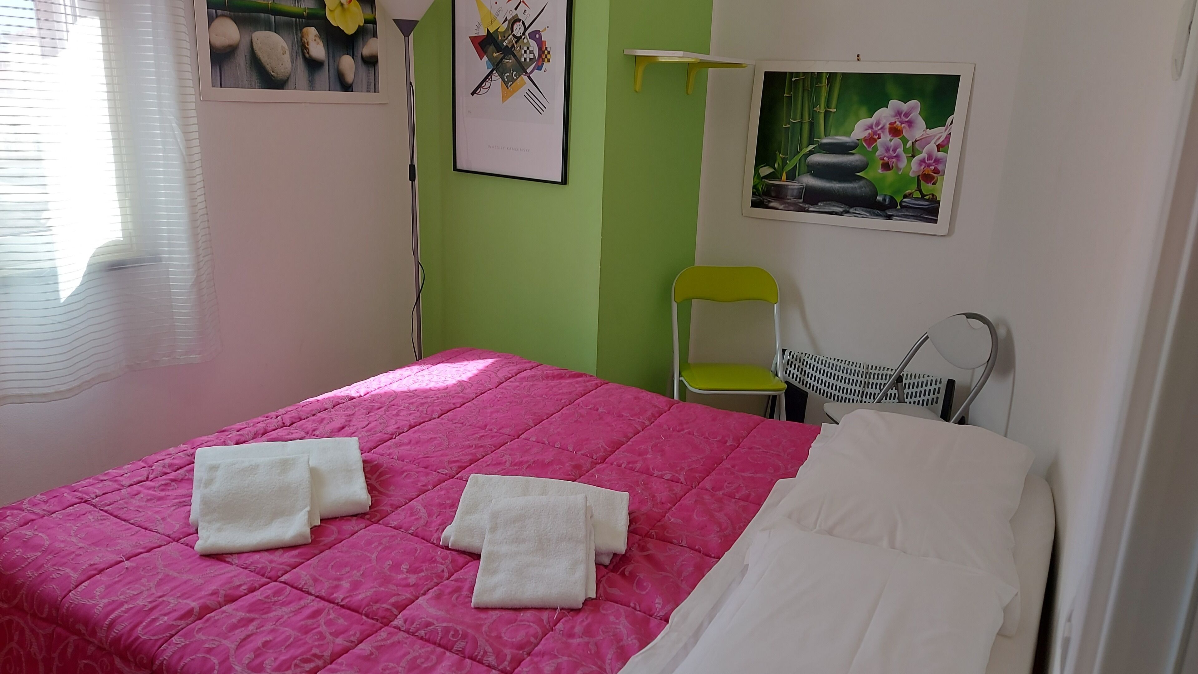 Una stanza con un letto, una sedia e un quadro appeso al muro.