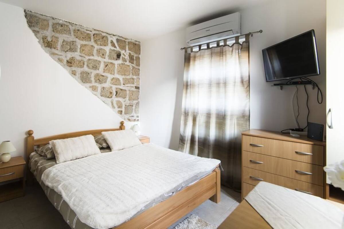 A bedroom with a stone wall, a bed, a TV, and a wooden dresser.
