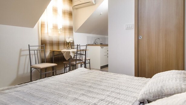 Un dormitorio con cama, escritorio y silla. Se observa una kitchenette al fondo.