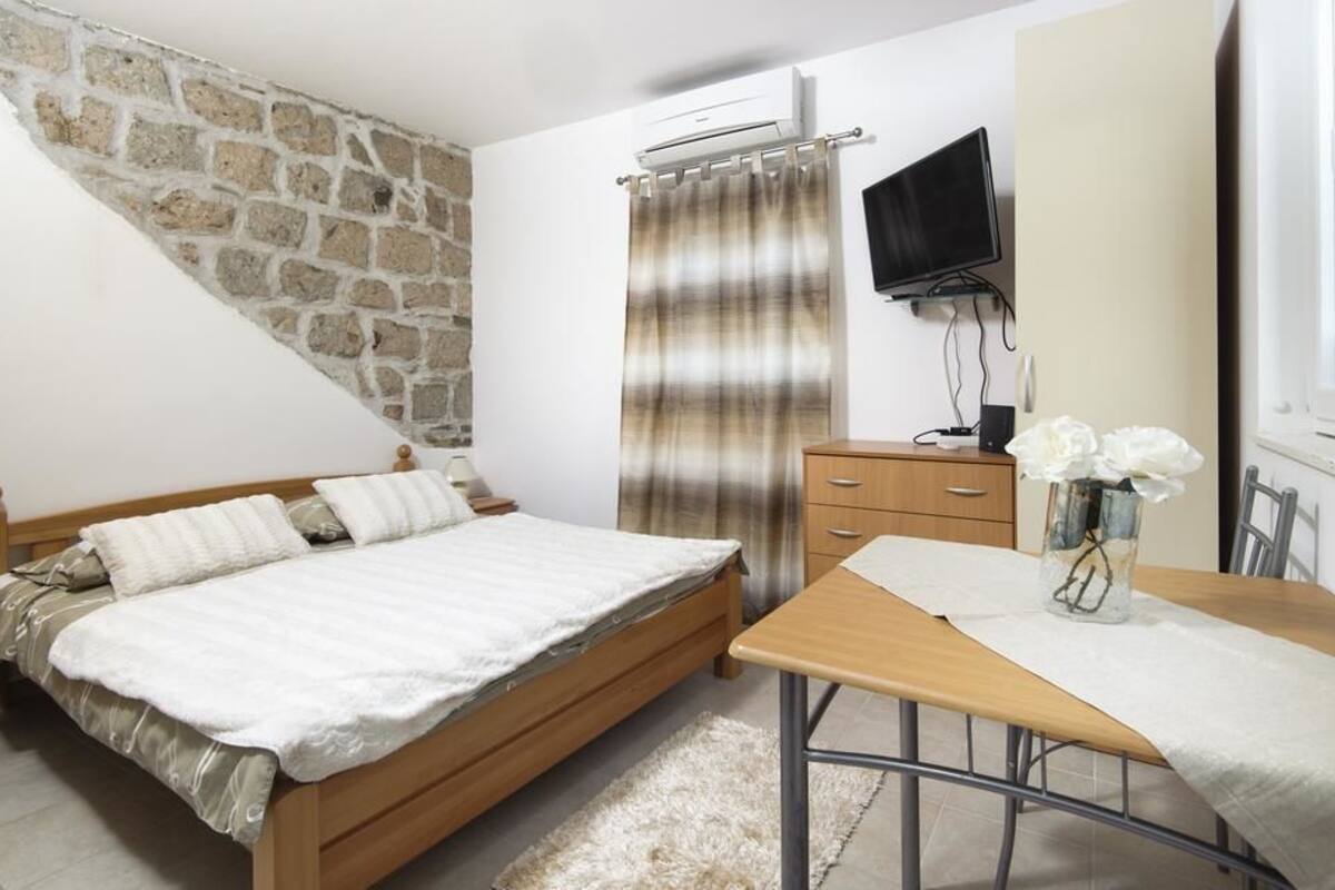 A bedroom with a bed, a wooden dresser, a TV, and a table with a vase of flowers.