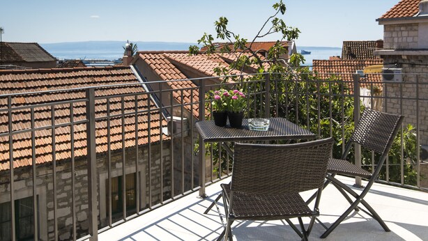 A balcony with a table and chairs, overlooking a cityscape with terracotta roofs and a view of the sea. - Nera Luxury Apartments (Split)