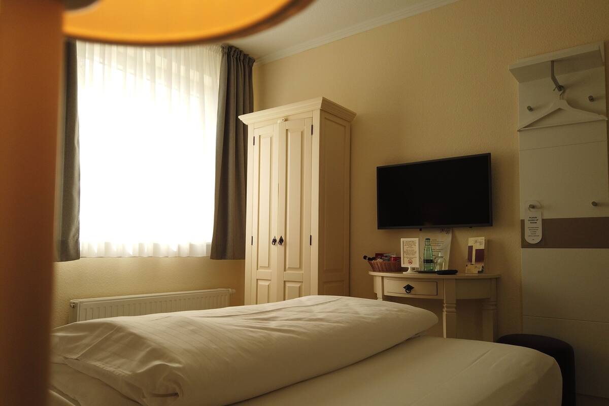 Une chambre d’hôtel comprenant un lit, une armoire, un bureau avec une télévision et une pancarte indiquant le type de chambre.