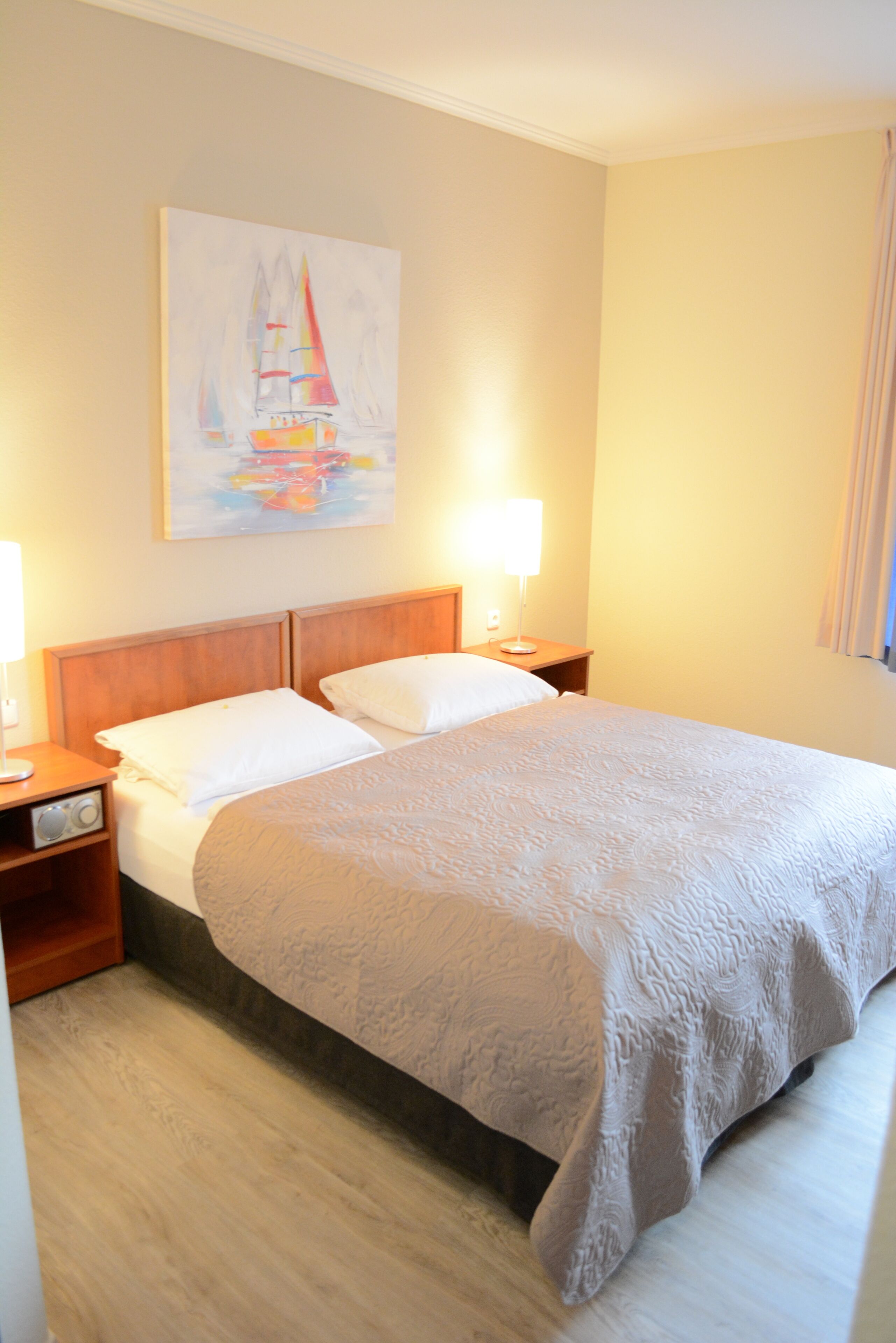 Habitación de hotel con una cama, dos mesitas de noche, una lámpara y un cuadro en la pared.
