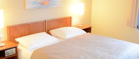 Habitación de hotel con una cama, dos mesitas de noche, una lámpara y un cuadro en la pared.