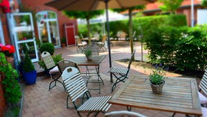 Eine Terrasse im Freien mit Holztischen und -stühlen, umgeben von Blumentöpfen und einem großen Sonnenschirm.